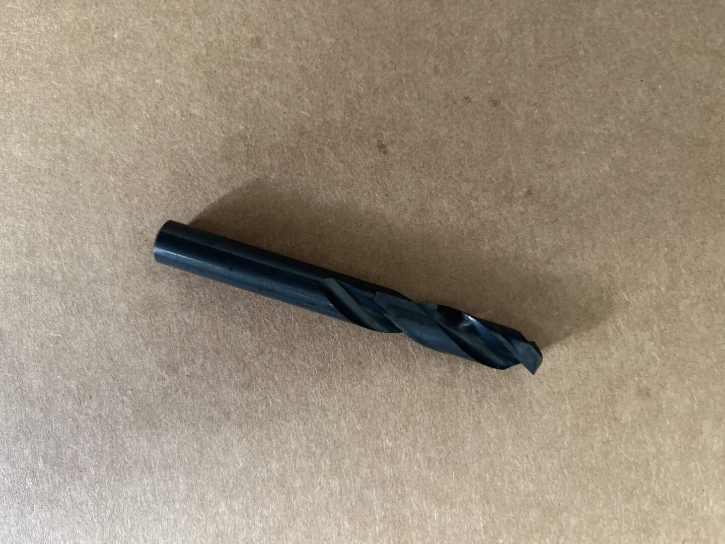 A black drill bit on a brown surface.